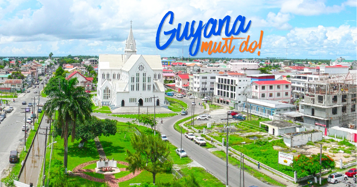 Aerial view of Georgetown, Guyana, featuring the iconic white St. George’s Cathedral surrounded by palm trees, city streets, and colorful buildings under a bright tropical sky, highlighting the charm and culture of Guyana’s capital city.