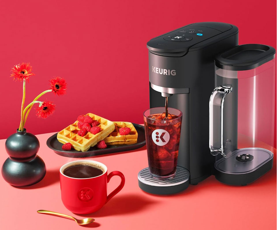 Matte black Keurig K-Supreme Gen 2 coffee maker brewing iced coffee next to a red mug and waffles.