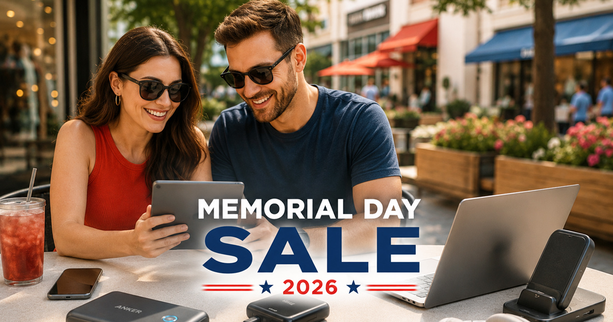 A smiling couple at an outdoor cafe looks at a tablet during a Memorial Day Sale, surrounded by technology including power banks and a laptop, on a bright, sunny day.