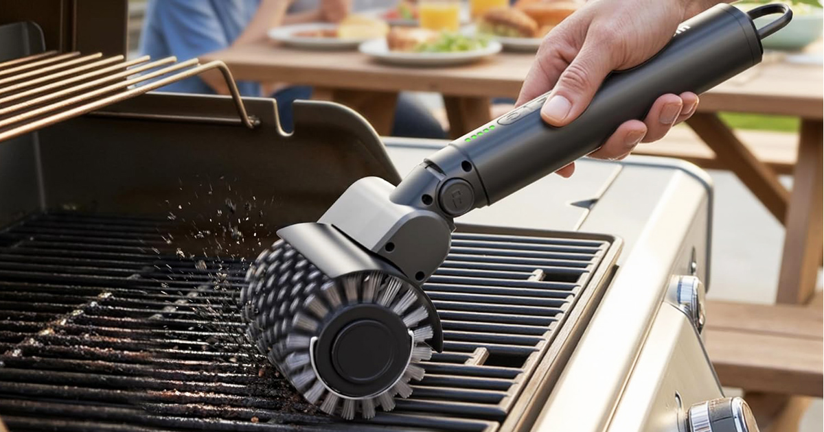 A cordless electric BBQ grill cleaning brush removing grease and burnt residue from outdoor grill grates during a backyard cookout.