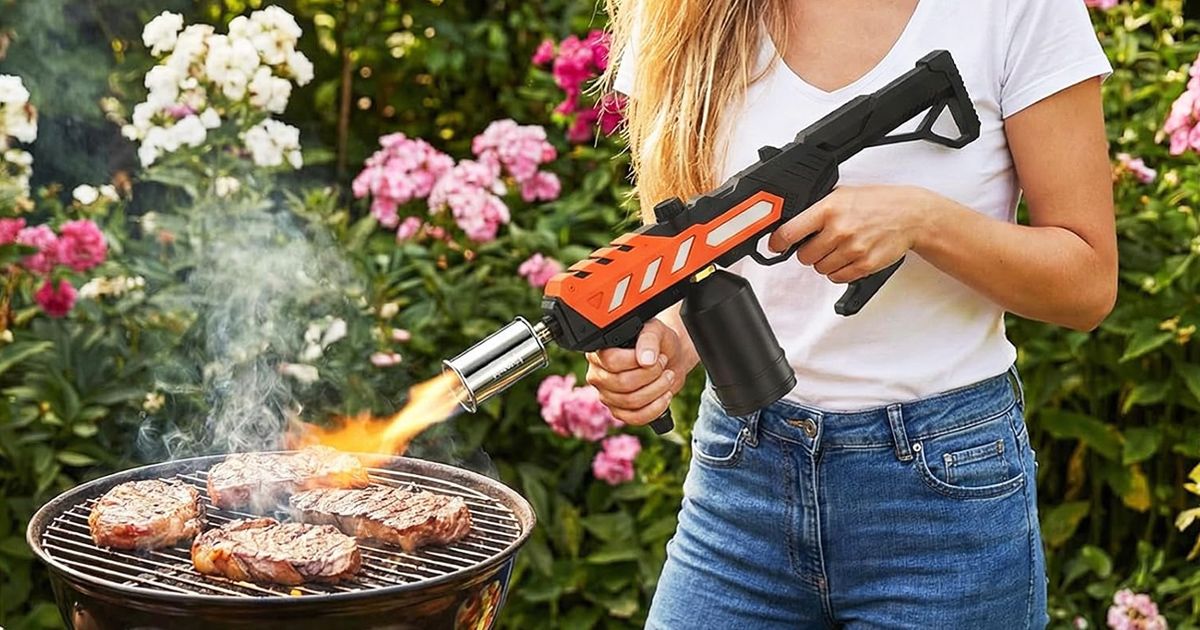 Woman using a powerful propane torch gun to sear steaks on an outdoor barbecue grill